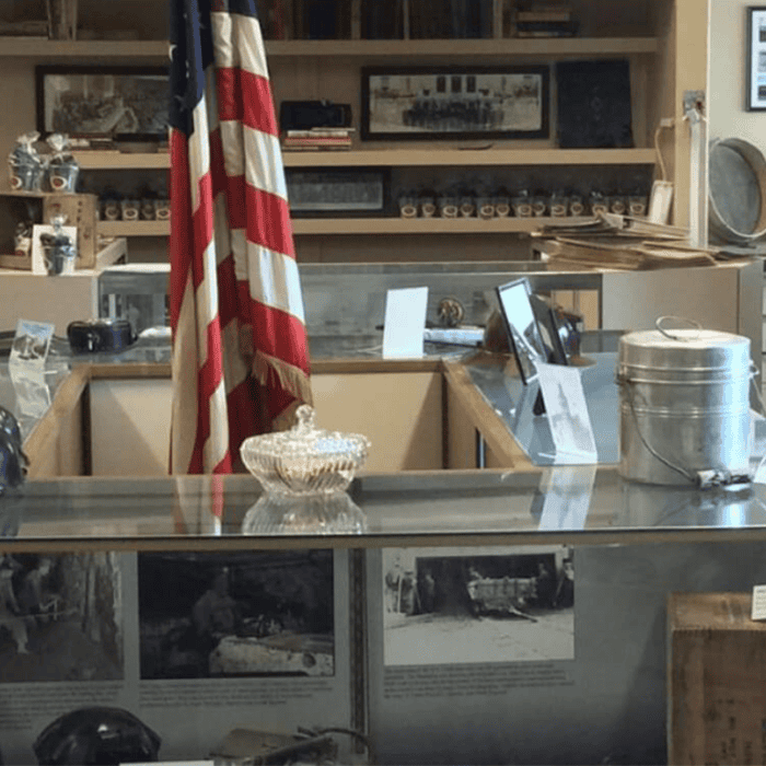 A glass display case with historical artifacts, a silver dish, and an American flag standing behind it in a museum setting.