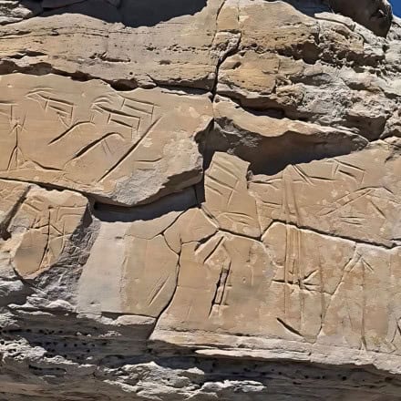 Rock wall with ancient petroglyphs featuring geometric shapes and figures carved into the stone surface.