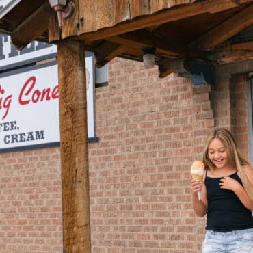 A woman and two children holding ice cream cones exit a building with a sign reading 