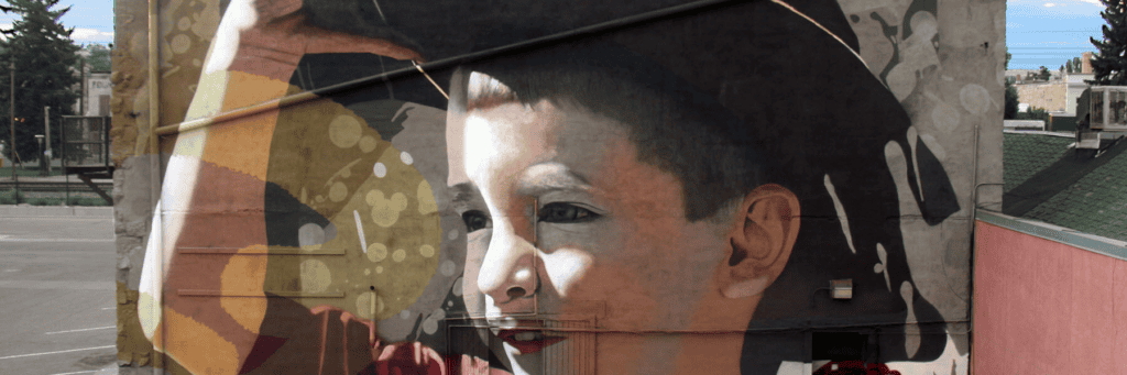 A large mural on a building wall depicts a young boy smiling and holding a hat above his head.