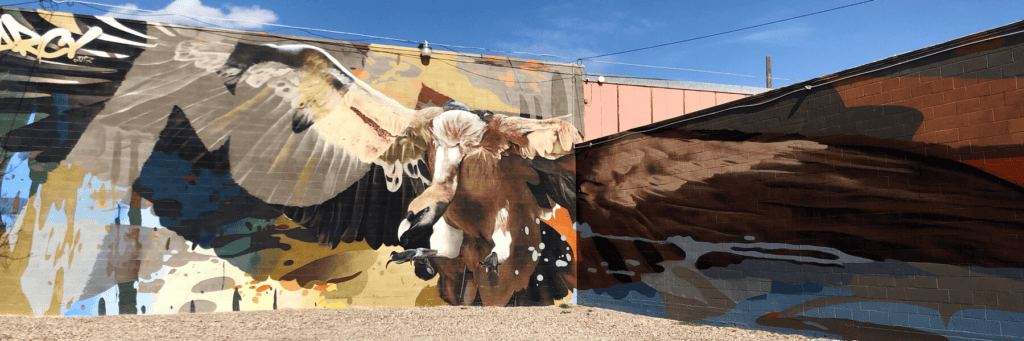 A large mural on a brick wall depicts a soaring eagle with wings fully spread, painted in natural brown and white tones against a colorful abstract background.