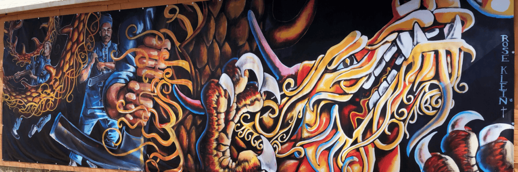 Colorful mural featuring a man with a sword fighting a dragon, with swirling flames and bold, dynamic lines. The artist’s name, Rose Klein, is visible on the right side.