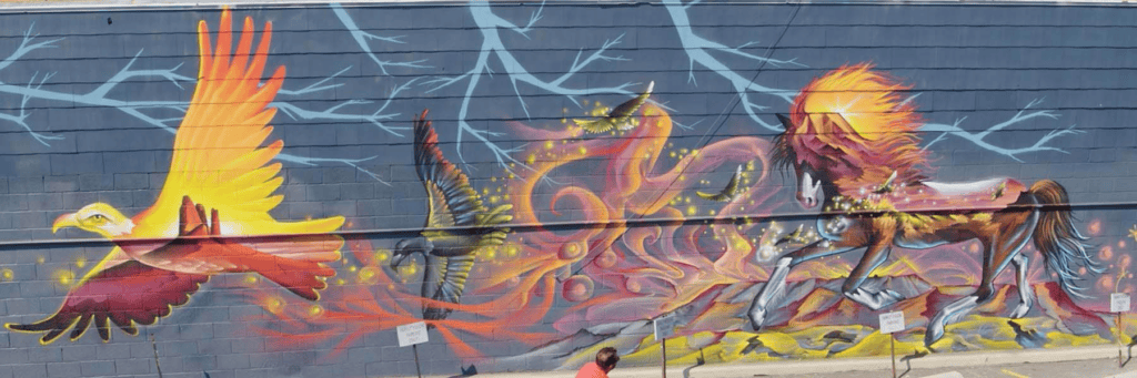 A mural shows a glowing yellow eagle, a flying green bird, and a fiery horse on a blue wall with lightning and swirling energy patterns.