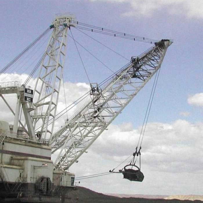 Large industrial dragline excavator with a suspended bucket is operating outdoors under a cloudy sky, positioned above a mound of earth.