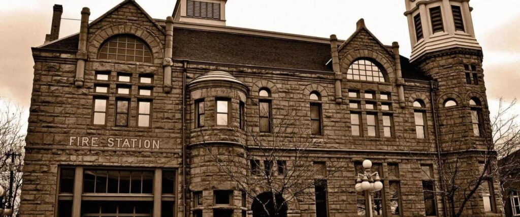 A historic stone fire station building with arched windows and a tall tower, photographed in sepia tones.