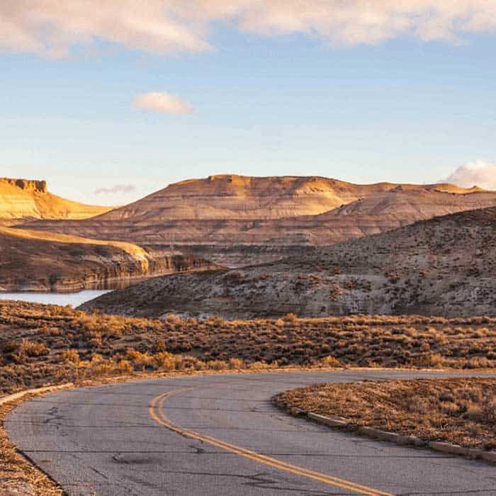 A paved road curves in the foreground, leading toward barren hills and a body of water under a partly cloudy sky.
