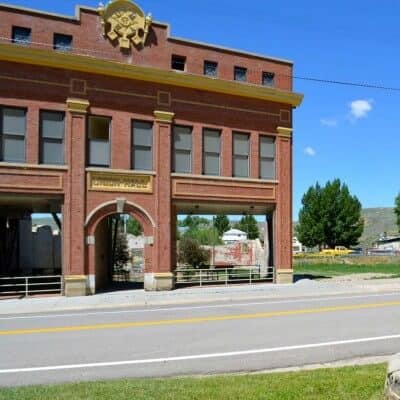 A two-story brick building with arched windows and a sign reading "City Hall" stands by an empty lot on a sunny day.