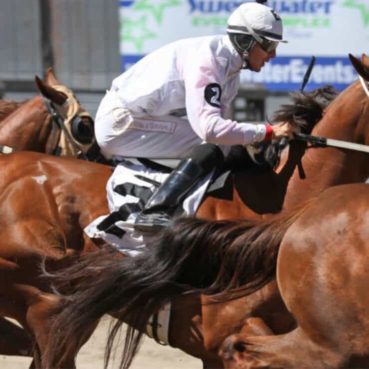 Jockeys ride racehorses in close competition on a dirt track during a horse race.