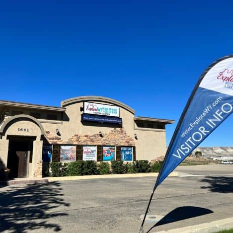 A tan building with signs for "Explore NV" and "Visitor Info" under a clear blue sky; a "Visitor Info" flag stands in front.