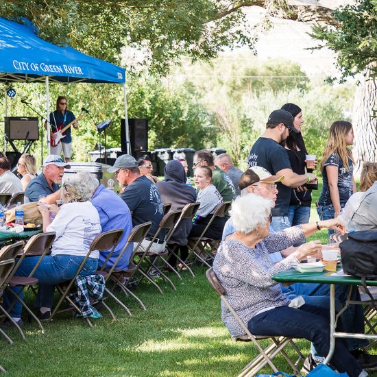 People sit at tables and eat under a blue 