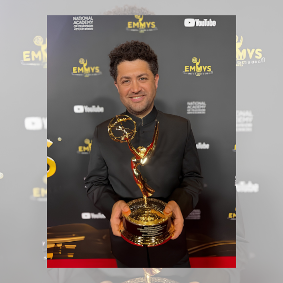 A man in a black suit holds an Emmy award in front of a backdrop with Emmy logos and sponsors.